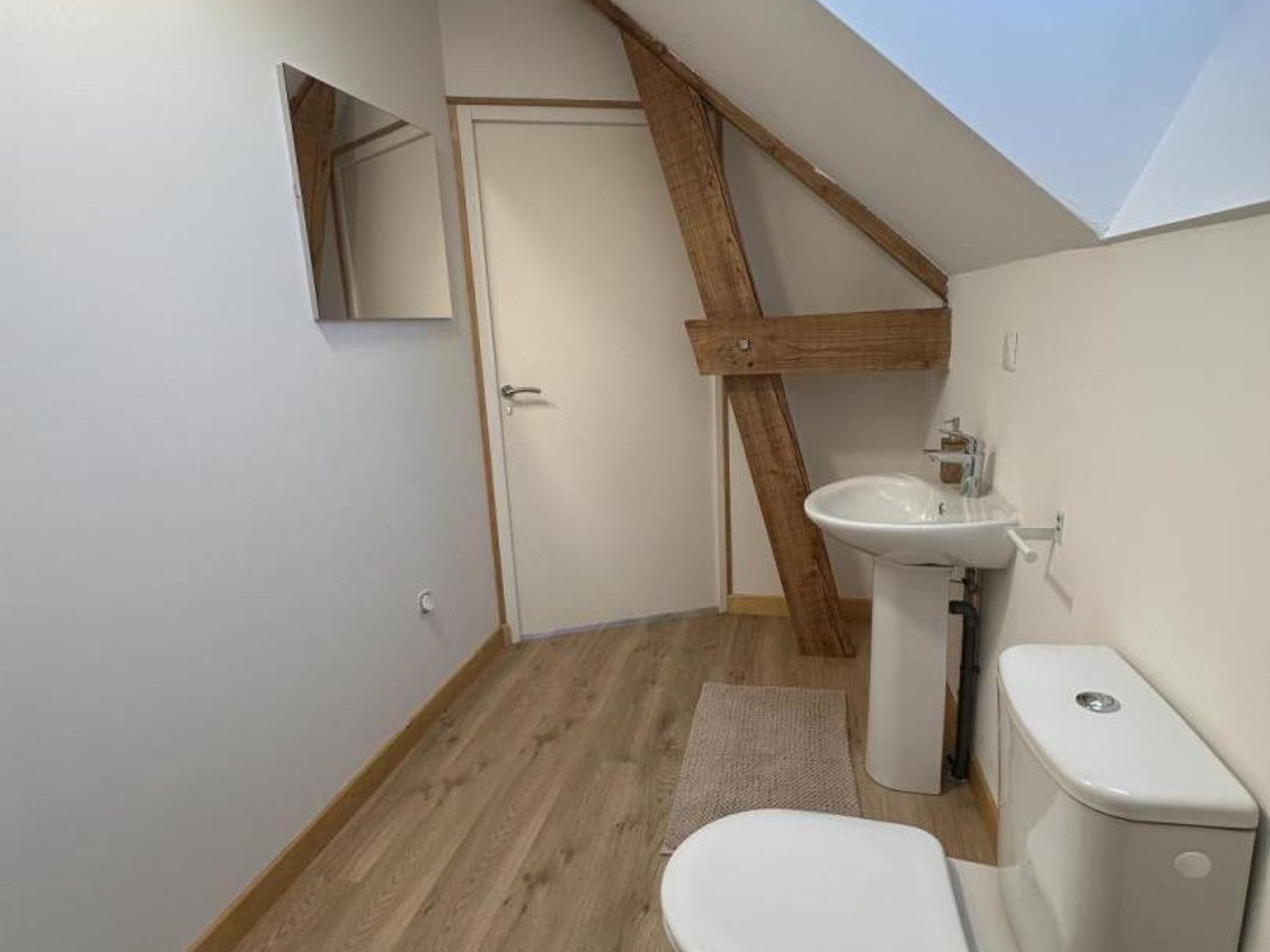 A small, compact bathroom with a wooden ceiling beam, a white sink, and a toilet.