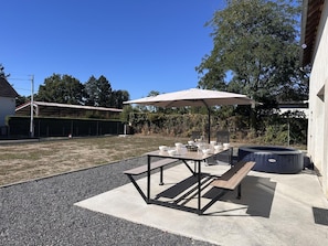 Eine Außenpatio-Terrasse mit Tisch, Stühlen, einem großen Sonnenschirm und einem Whirlpool.
