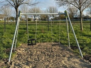 A swing set in a park with a grassy area and trees in the background. - Mobile home with AC - 6 guests (Arvert)