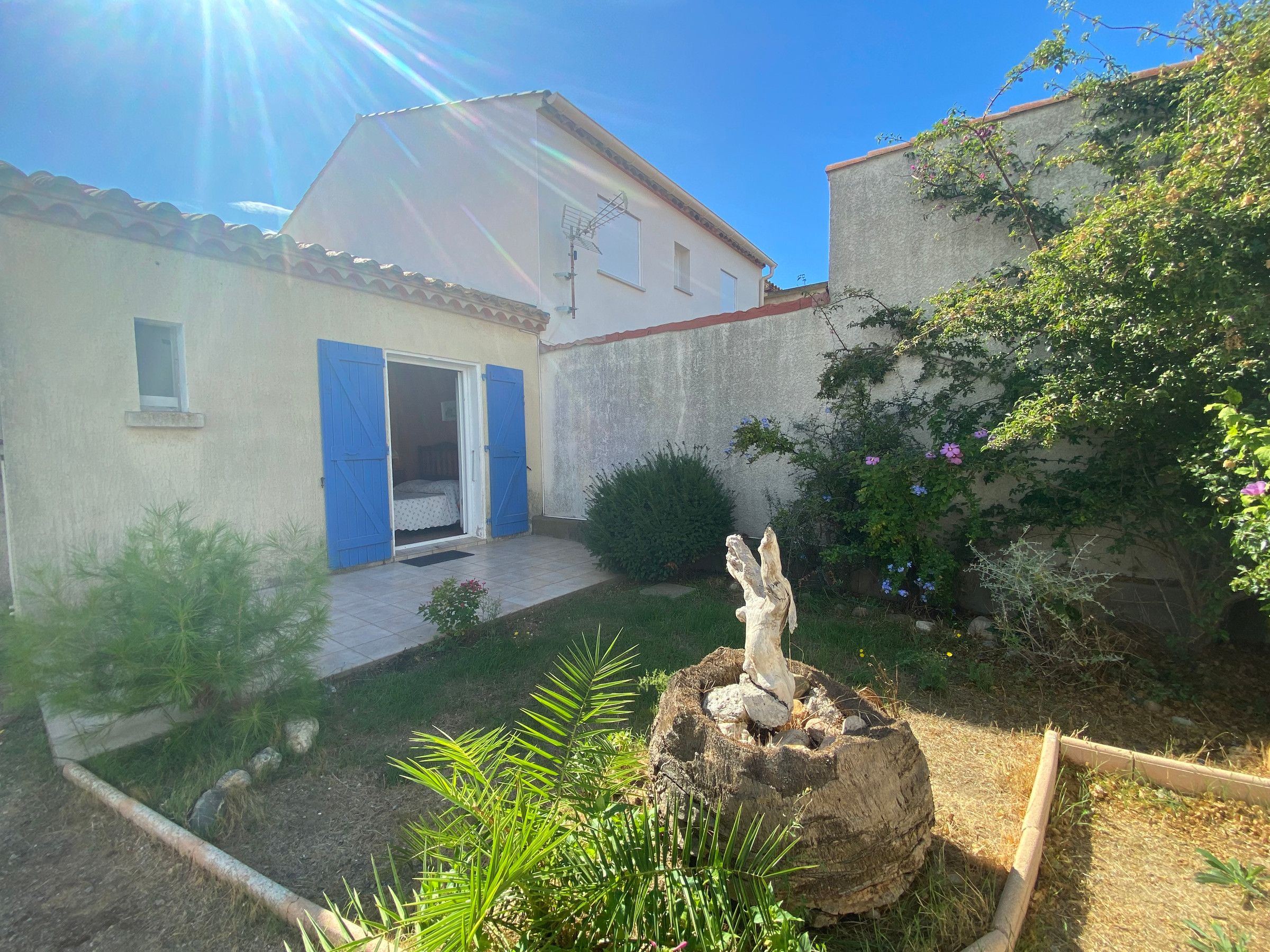 Une propriété résidentielle dotée d’un jardin, d’une sculpture en bois et d’une maison aux volets bleus.