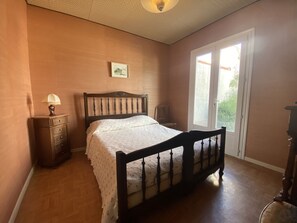 Ein Schlafzimmer mit einem hölzernen Bett, einem Nachttisch, einer Lampe, einer Kommode und einem Fenster mit Blick.