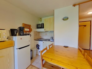 Eine kompakte Küche mit Kühlschrank, Mikrowelle, Kaffeemaschine und Waschmaschine.