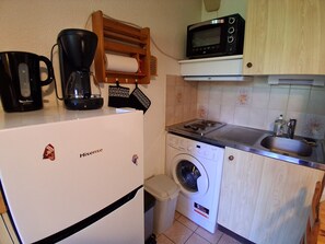 Ett kompakt kök med kylskåp, mikrovågsugn, kaffebryggare och tvättmaskin.