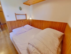 Ein Einzelbett mit Holz Kopfteil und weißer Bettwäsche in einem Raum mit Holzboden und schräg versiegelter Decke.