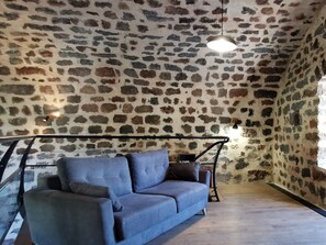 Een kamer met een stenen muur, een blauwe bank en een hangende lamp.