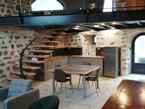 Une cuisine compacte avec un coin repas, un escalier et une vue sur l’extérieur, visible à travers une porte en arc de cercle.