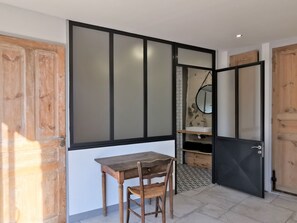 Een kamer met een houten deur, een tafel met een stoel, een spiegel en een betegelde vloer.