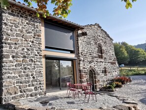 A stone building with a modern glass door and a patio area with red chairs. - Country house - Arsac-en-Velay (Arsac-en-Velay)