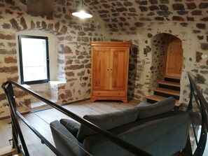 A room with a stone wall, a wooden cabinet, a sofa, and a staircase with a wooden door. - Country house - Arsac-en-Velay (Arsac-en-Velay)