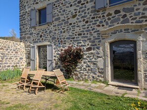 A stone building with a patio area featuring wooden chairs and a table. - Tranquil manor house - 11 guests (Arsac-en-Velay)