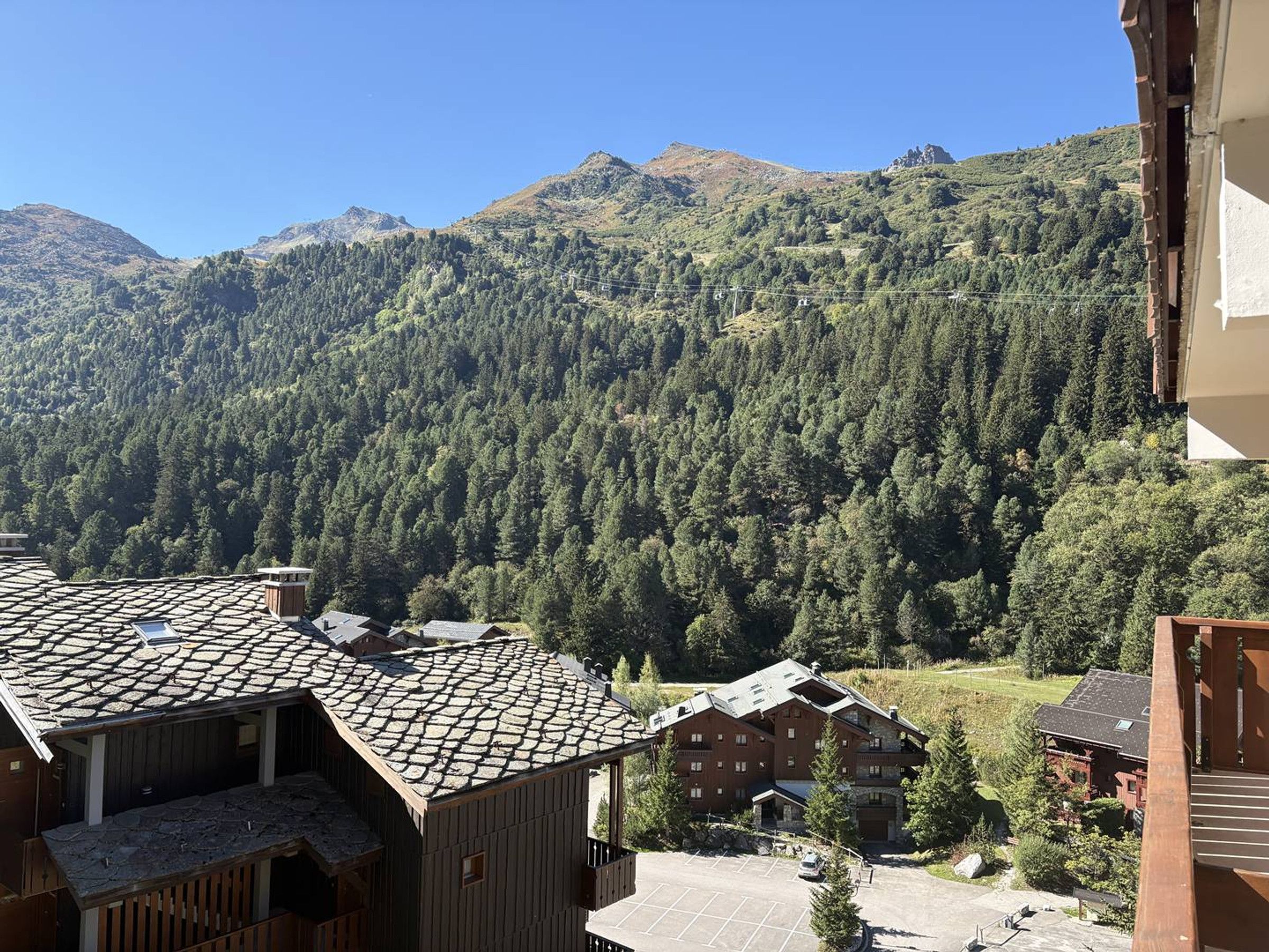 A mountain lodge with a parking area and a view of forested mountains.