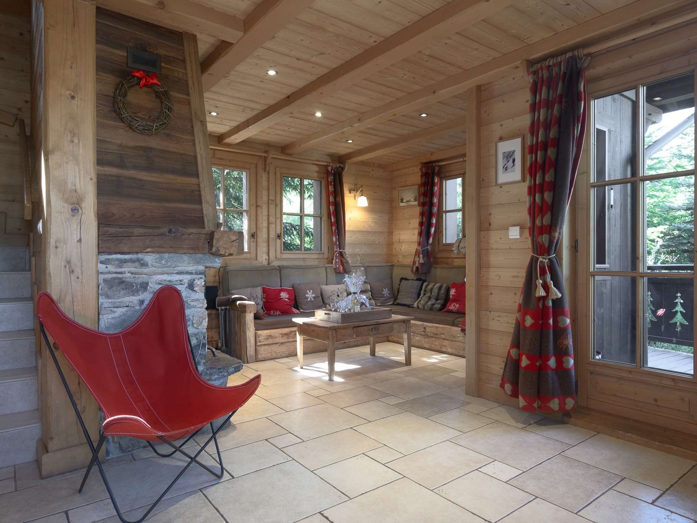 A log cabin interior with a fireplace, a red chair, a sofa, and a dining table.