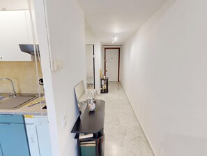 A narrow hallway with a kitchen area on the left, a dining table with chairs, and a door at the end. - Studio with AC and terrace - 2 guests (Menton)