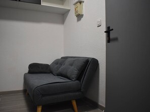 A corner room with a grey sofa, a small white shelf, and a door with a black handle. - Studio cabin near slopes - 3 guests (Bolquère)