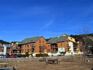 A row of multi-story residential buildings with balconies, a parking area, and a picnic table in the foreground. - Studio cabin near slopes - 3 guests (Bolquère)