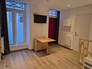 A room with a wooden desk, a television mounted on the wall, and a red door. - Central studio - 4 guests (Cauterets)