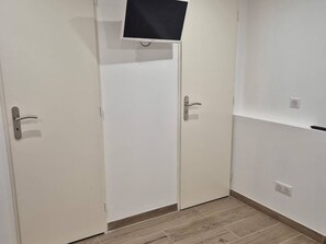 A room with two white doors, a mounted television, and a wooden floor. - Central studio - 4 guests (Cauterets)