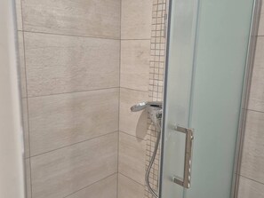 A corner of a room with beige tiled walls and a glass shower door with a metal handle. - Central studio - 4 guests (Cauterets)