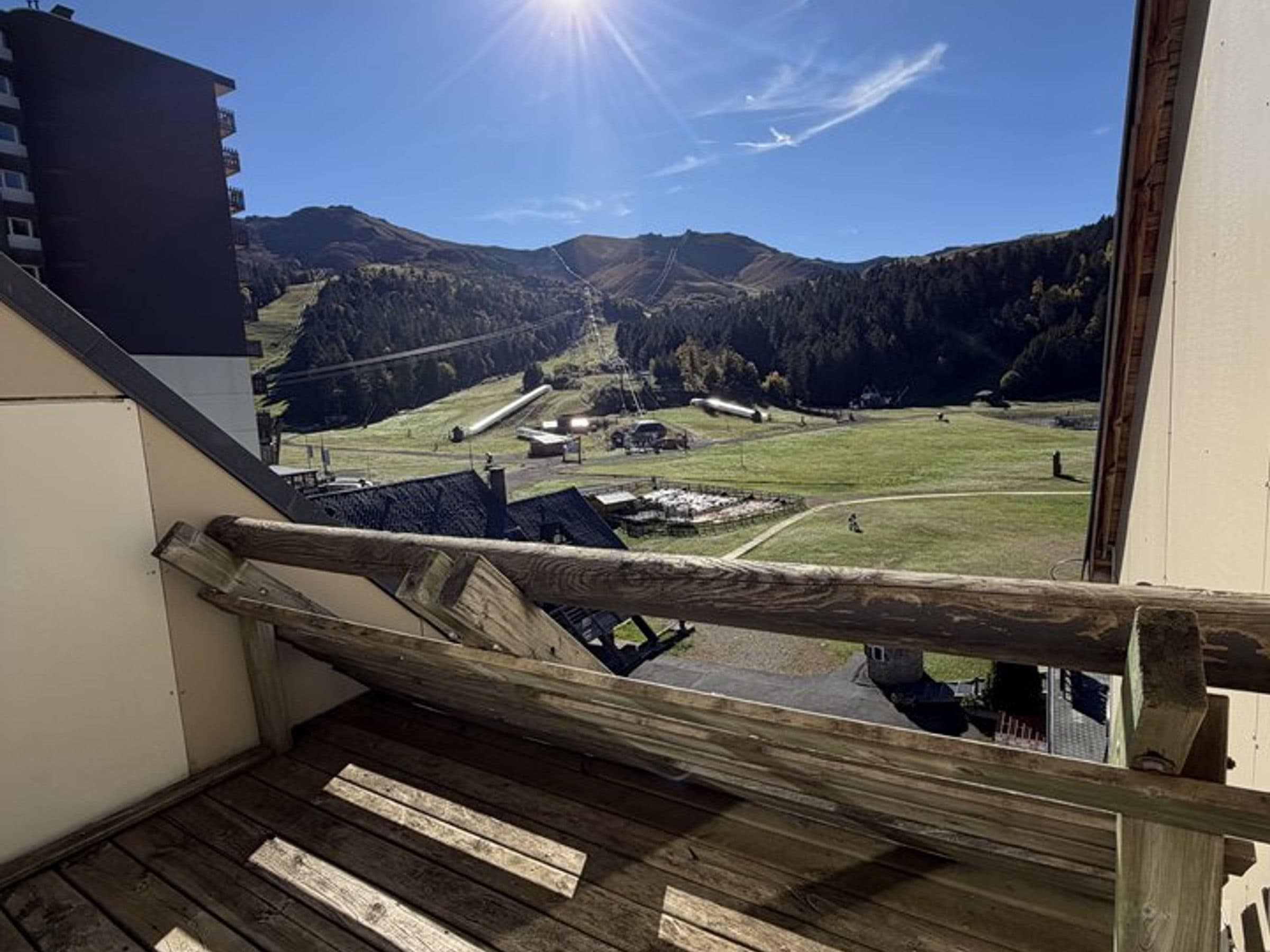 Un escalier en bois mène à un balcon d’où l’on peut admirer un paysage montagneux sous un ciel dégagé.