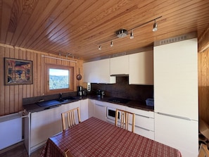 A compact kitchen with wooden paneling, a dining table with chairs, and a window with a view. - Duplex apartment in the resort center - 7 to 9 guests. (Le Lioran)