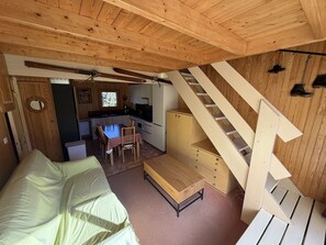 Un espacio habitable compacto con una cama, una mesa de comedor, una zona de cocina y una escalera.