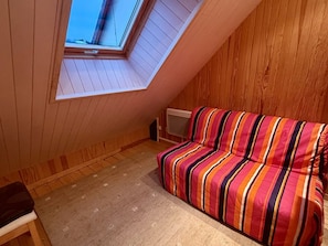 A small room with a sloped ceiling, a wooden wall, a colorful striped sofa, a small table, and a radiator. - Duplex apartment in the resort center - 7 to 9 guests. (Le Lioran)