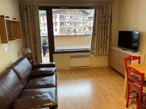 A living room with a leather sofa, a dining table with a red chair, a television, and a window with curtains. - Studio in the center - 4 guests (Pralognan-la-Vanoise)