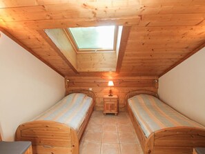 Een knusse kamer met twee houten bedden, een dakraam en een nachtkastje met een lamp.