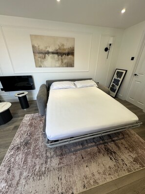 A modern bedroom with a bed, a flat-screen TV, a side table, and a painting on the wall. - Apartment - Sleeps 2 - Parking - Garden - Seaside (Rochester)