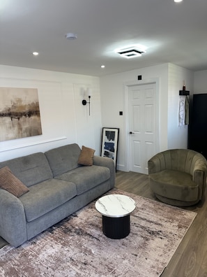 A modern living room with a grey sofa, a round coffee table, and a beige armchair. - Apartment - Sleeps 2 - Parking - Garden - Seaside (Rochester)