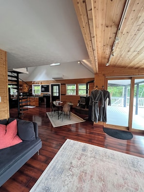 A spacious living area with a wooden floor, a sofa, a dining table with chairs, a television, and a staircase leading to an upper level. - EmberGlow Cabin — Mountaintop Retreat  Outdoor Soaking Tub, Firepit & Starlink (Rio)