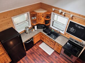 A compact kitchen with wooden cabinetry, a black refrigerator, a microwave, a sink, and a stove. - EmberGlow Cabin — Mountaintop Retreat  Outdoor Soaking Tub, Firepit & Starlink (Rio)