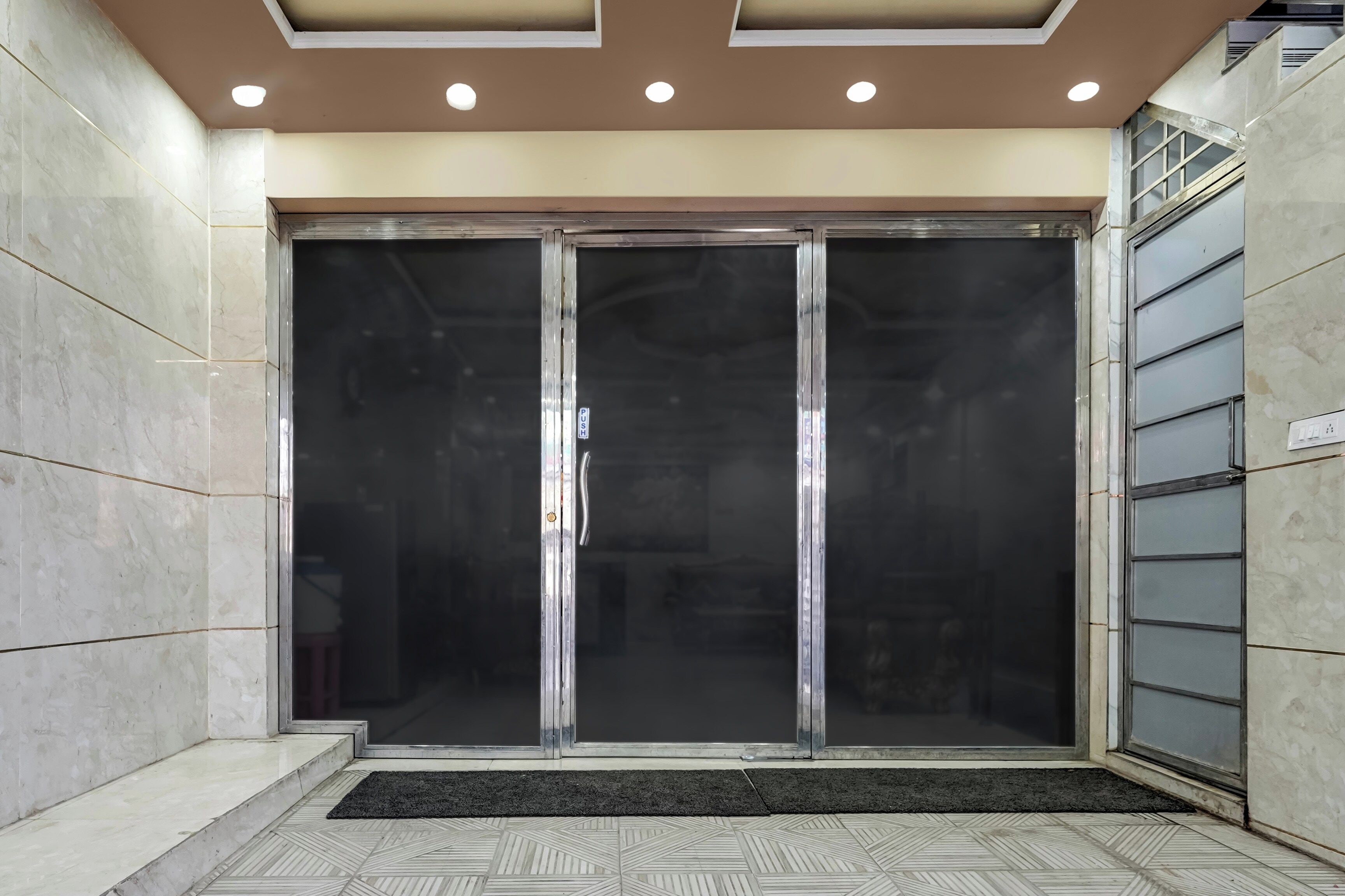 A hotel entrance with a glass door, a tiled floor, and a ceiling with recessed lighting.