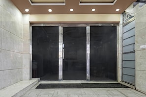 Entrada de un hotel con puerta de cristal, suelo de baldosas e iluminación empotrada en el techo.