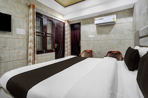 Habitación de hotel con cama, una silla de madera, aire acondicionado de pared y televisor.