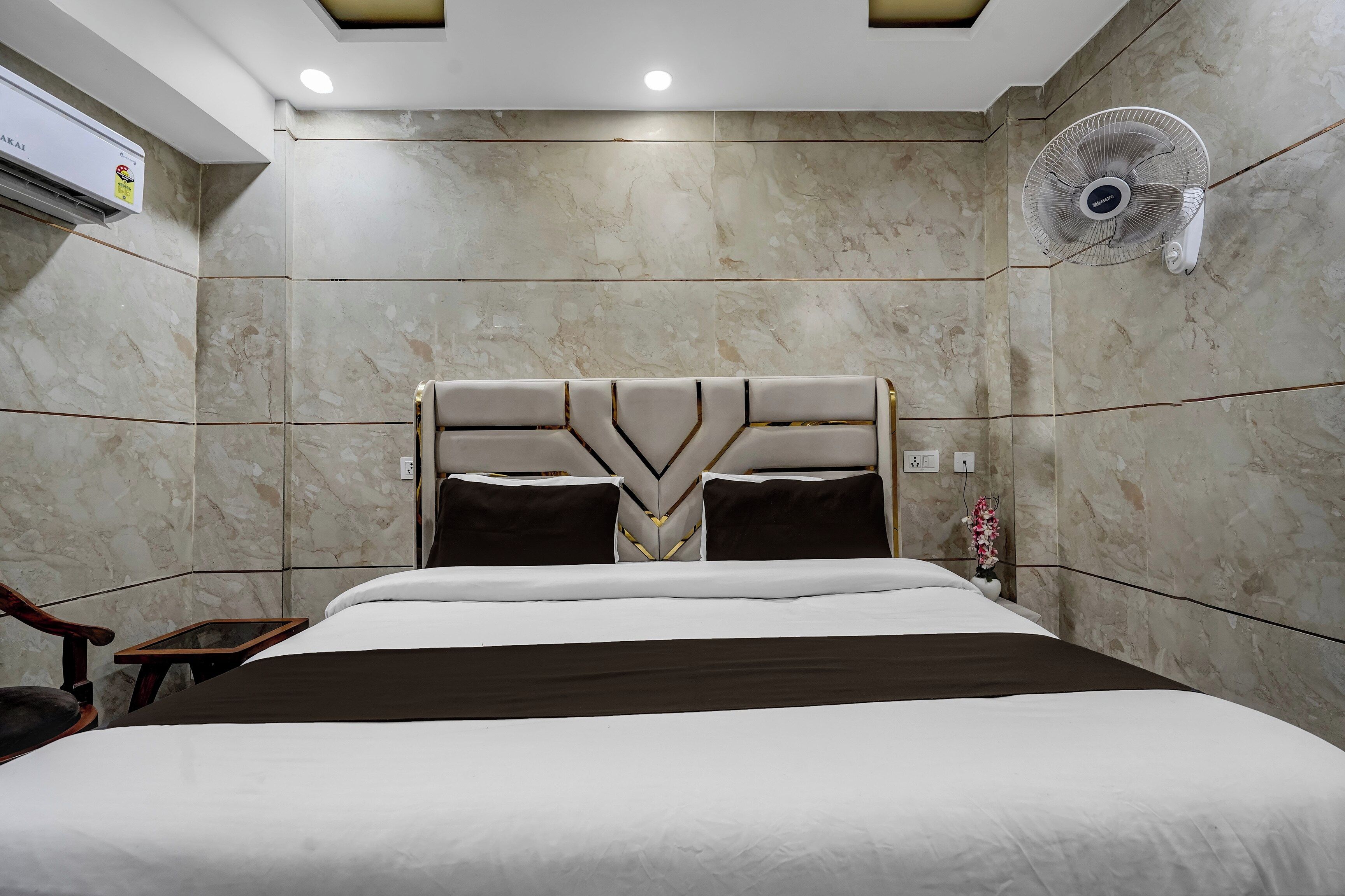 A hotel room with a bed, a wall-mounted fan, and a marble-patterned wall.