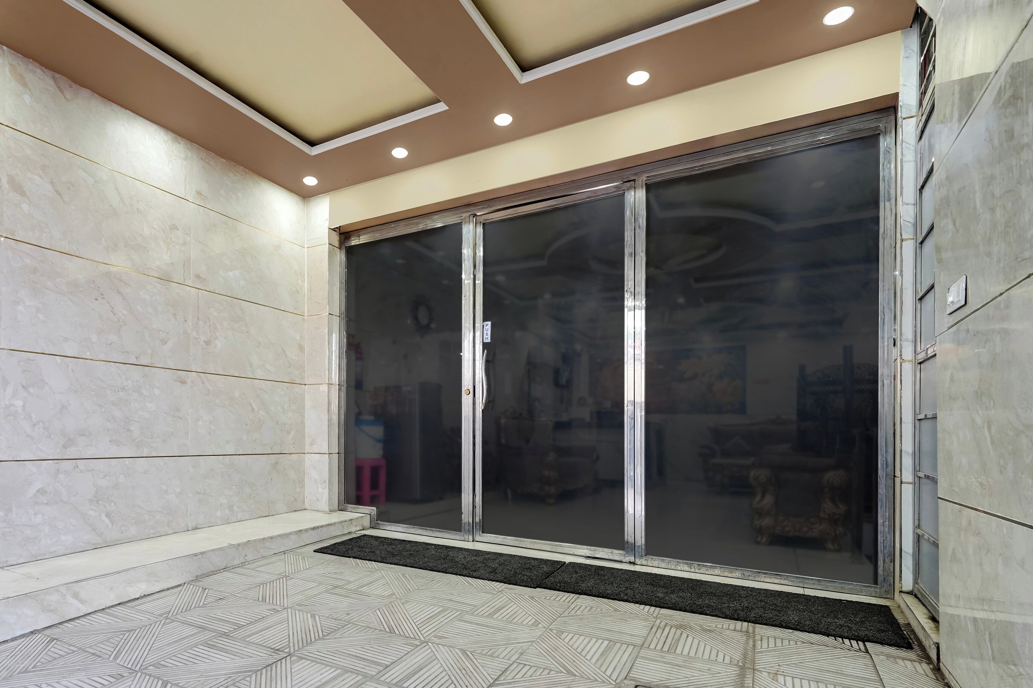 A hotel entrance with a tiled floor, a glass door, and a ceiling with recessed lighting.