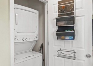 A laundry room with a white washer and dryer, a door organizer with storage baskets, and a metal drying rack. - Spacious Coastal Home with Gulf View Balcony. 3 beach accesses & park. 3BR/3BA (Port St. Joe)