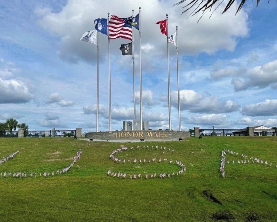 Une zone herbeuse avec un monument portant l’inscription « ALLÉE DU SOUVENIR » et plusieurs drapeaux.