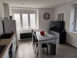 Eine moderne Küche mit Essbereich, einem großen Fenster mit Milchglas, einer Wanduhr und einem Fernseher.