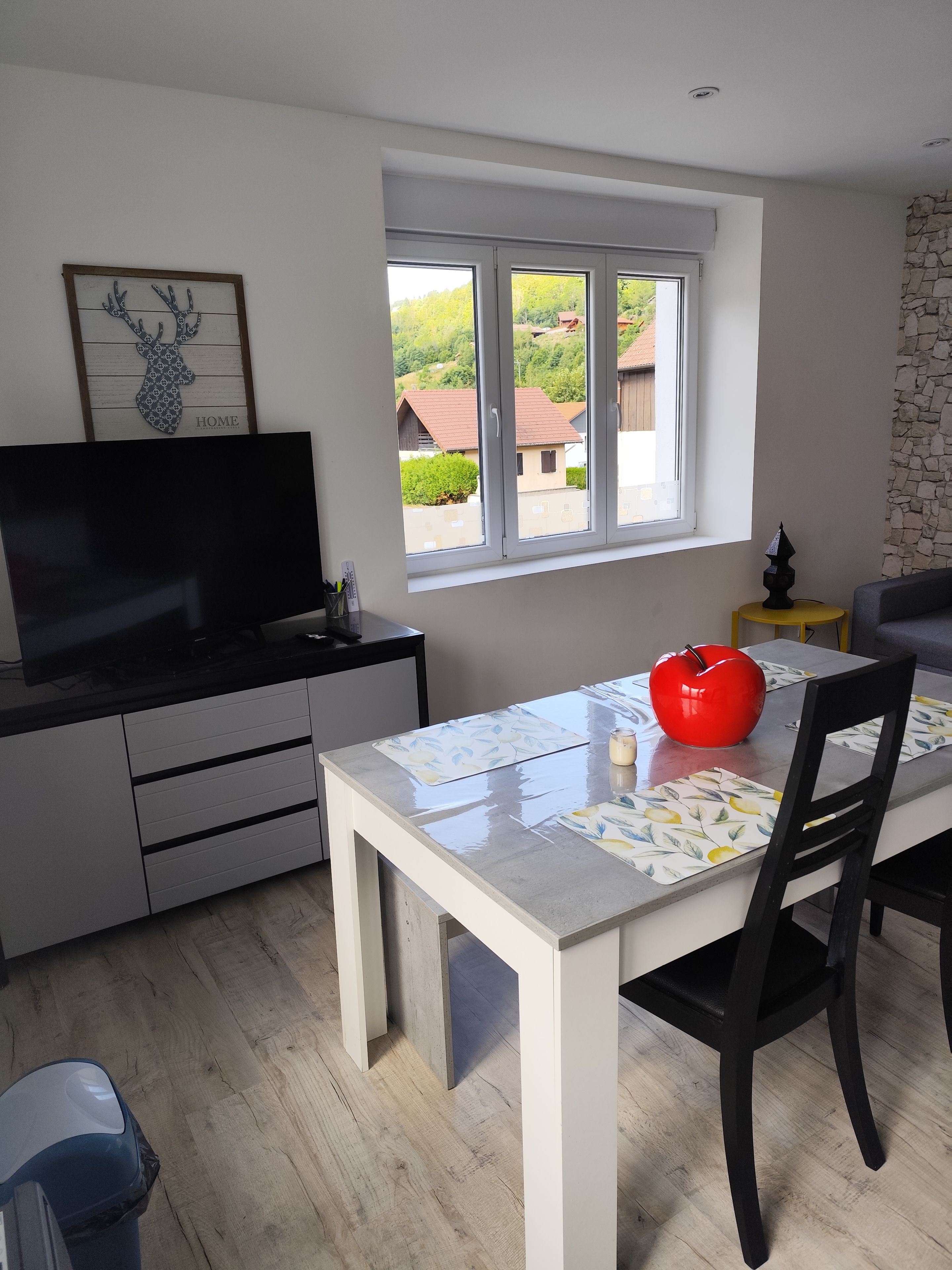 Una cocina moderna con una mesa de comedor, sillas, un televisor y una ventana con vistas a casas.