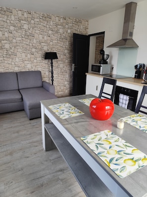 Ein moderner Wohnraum mit Steinwand, einem grauen Sofa, einem Esstisch mit Zitronenmuster-Platzsets und einem roten Salatkernchen auf dem Tisch.