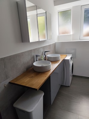 Ein modernes Badezimmer mit Holztischplatte, zwei Waschbecken, einer Waschmaschine und einem großen Spiegel.