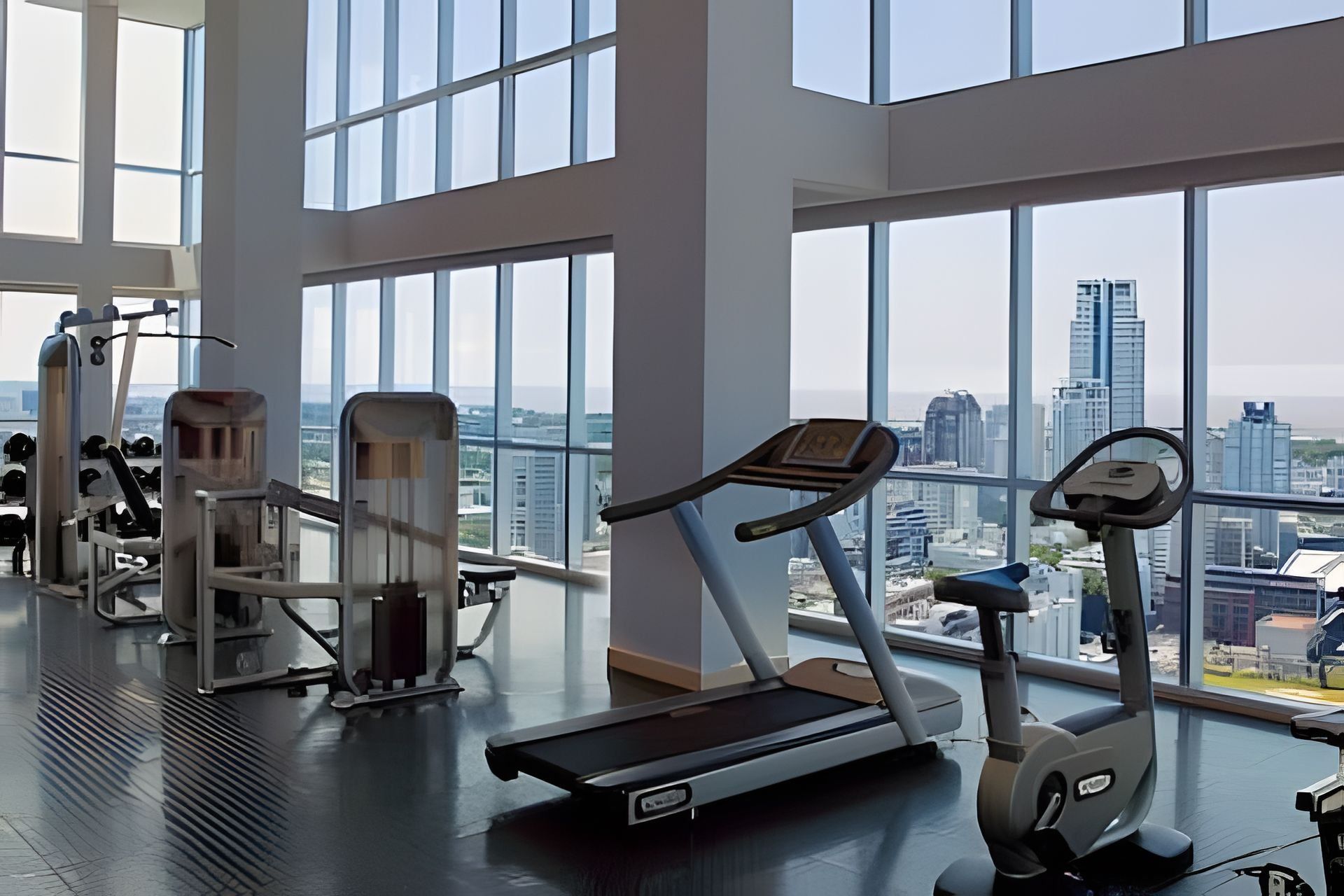 A gym with exercise equipment and large windows offering a city view.