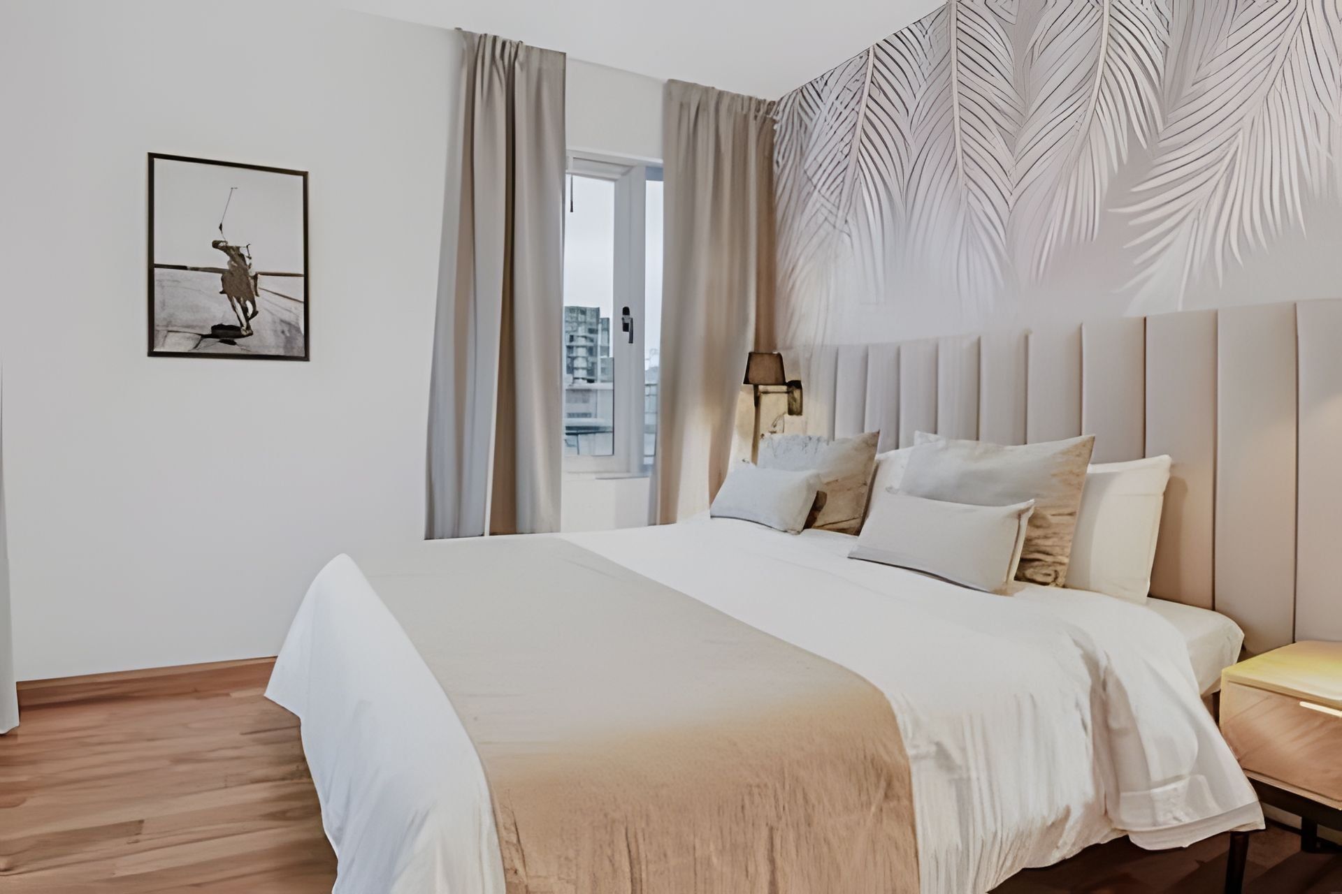 A modern bedroom with a large bed, a nightstand, a lamp, and a city view.