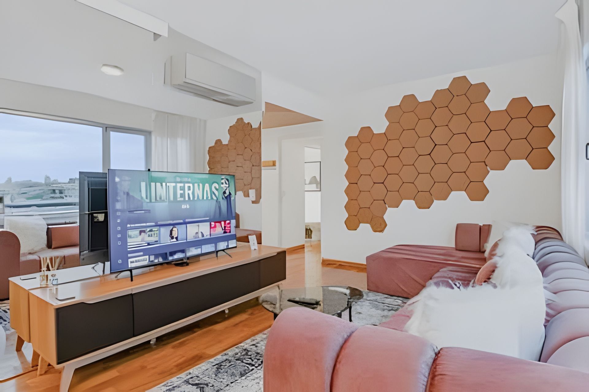 Una sala de estar moderna con un televisor de pantalla plana grande, un sofá, una mesa de centro y una decoración hexagonal única en la pared.