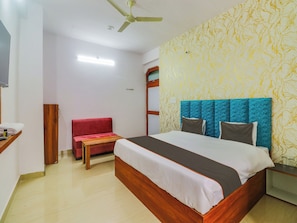 A hotel room with a bed, a red bench, a wooden nightstand, and a ceiling fan.