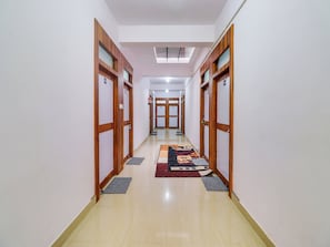 A hotel hallway with wooden doors, a patterned rug, and a tiled floor.
