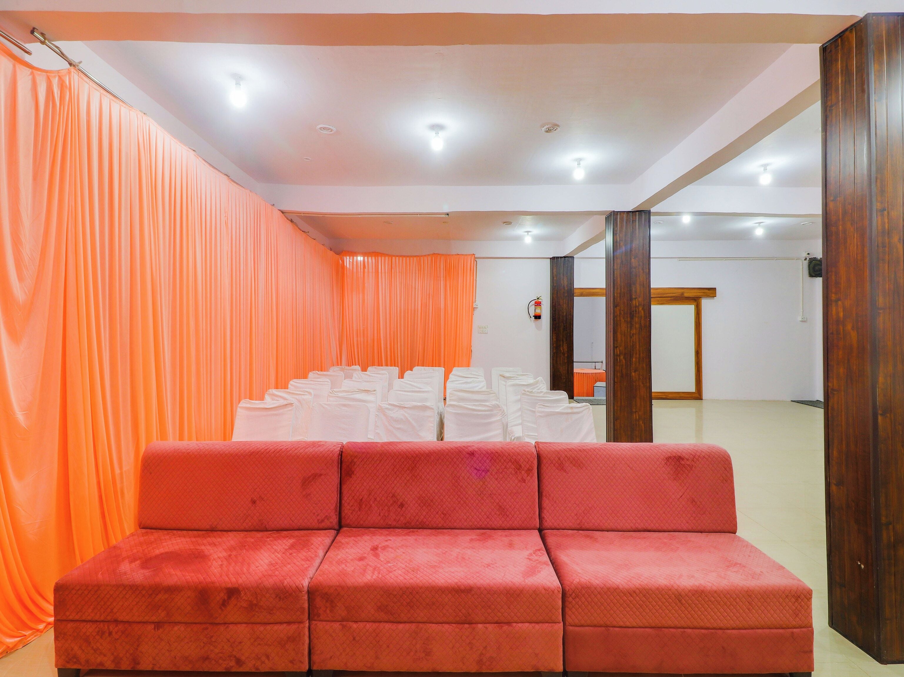Una habitación con un sofá rojo, sillas blancas y cortinas naranjas.