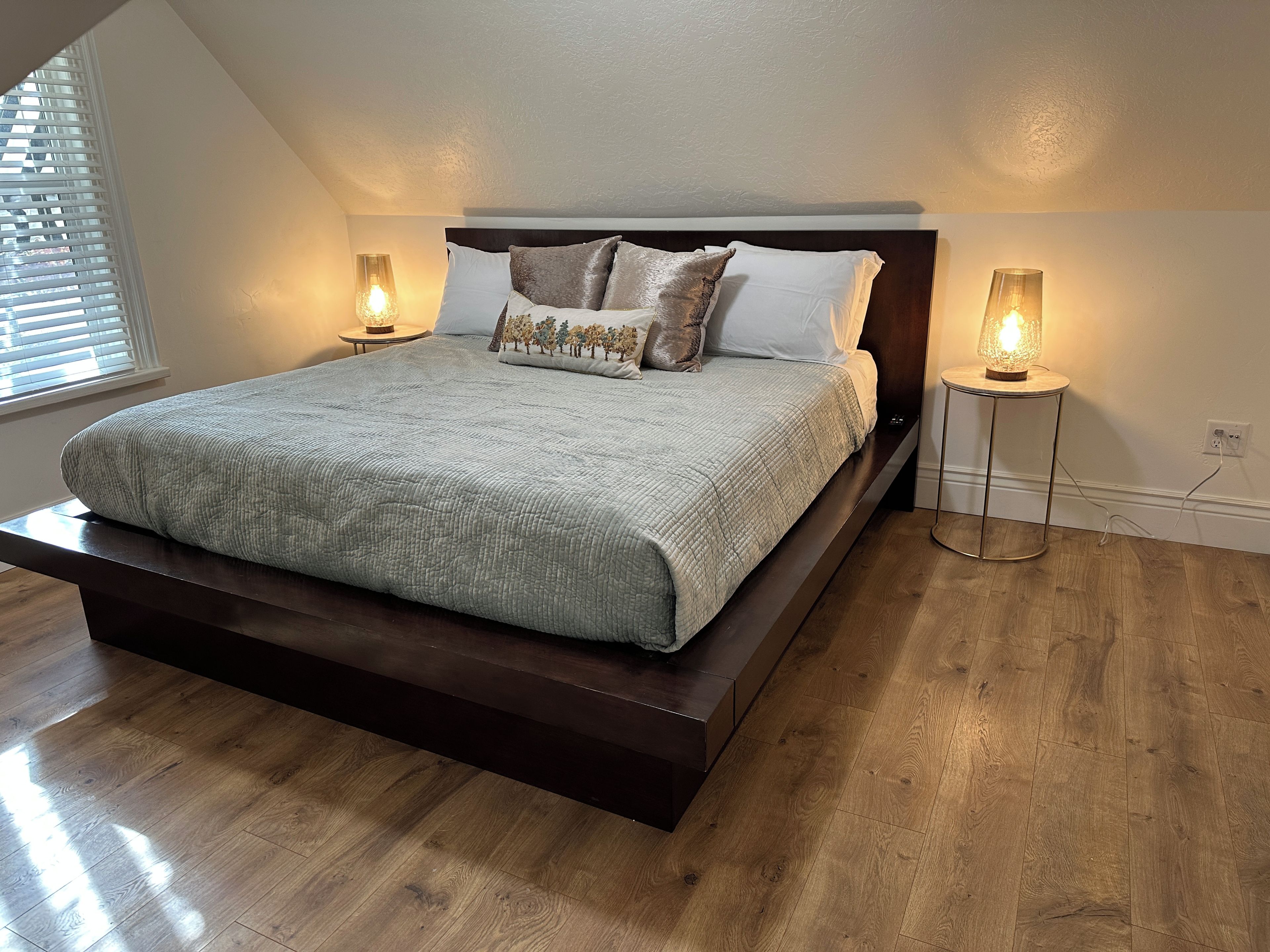 A bedroom with a large bed, two bedside lamps, and a window with blinds.